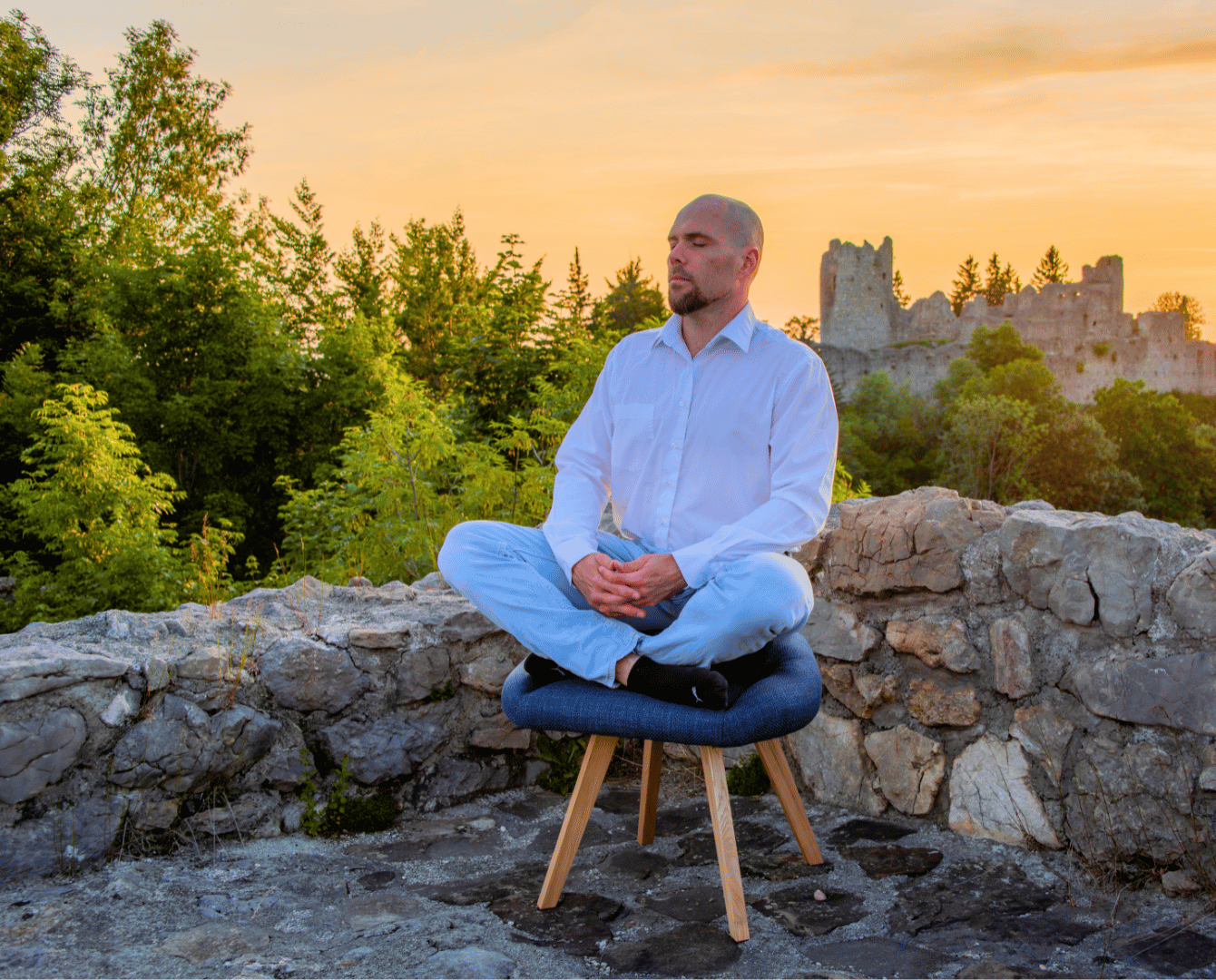 Mann sitzt auf blauem Stuhl für den Schneidersitz, vor Burgruine