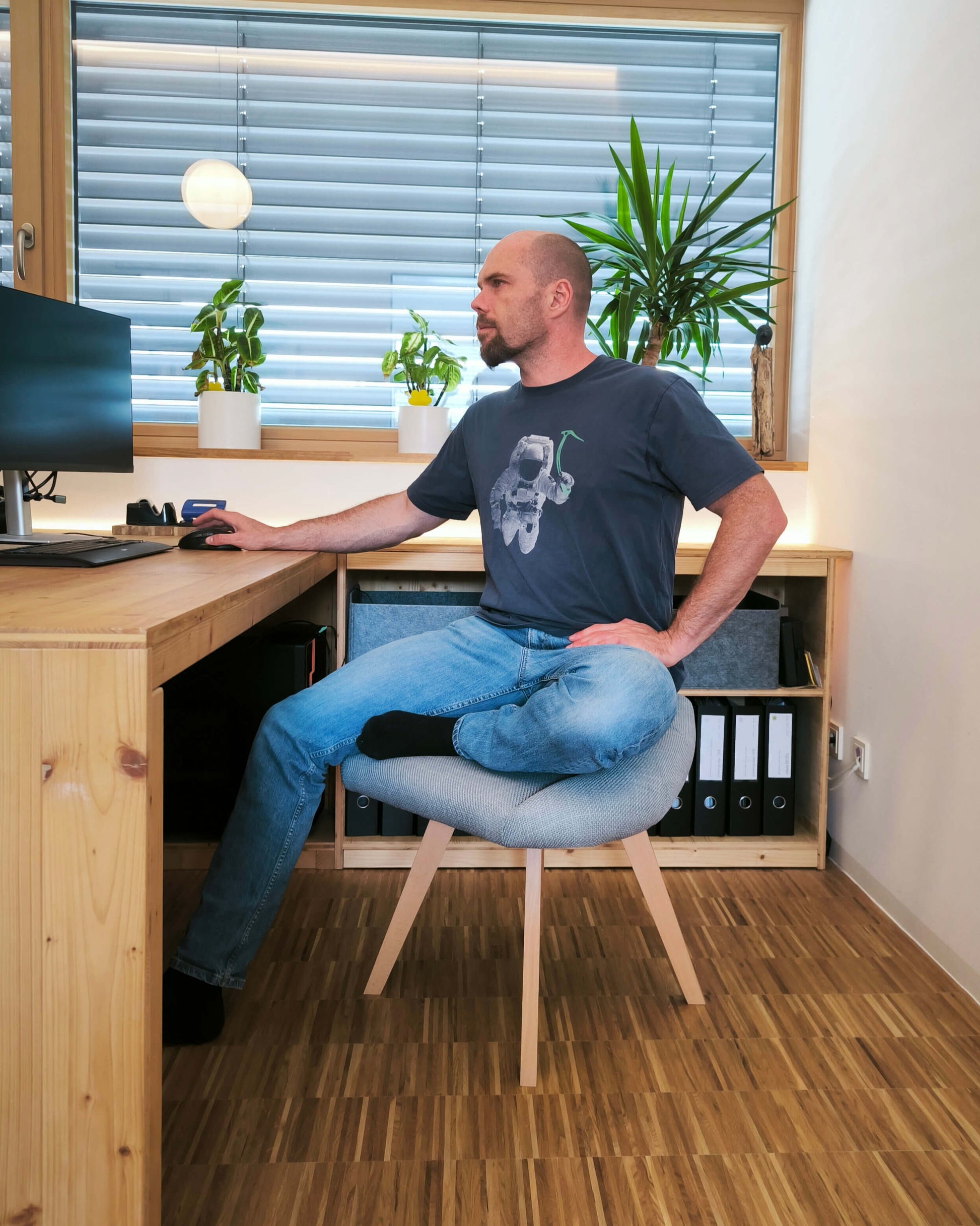 Mann sitzt am Schreibtisch auf grauem Stuhl für den Schneidersitz