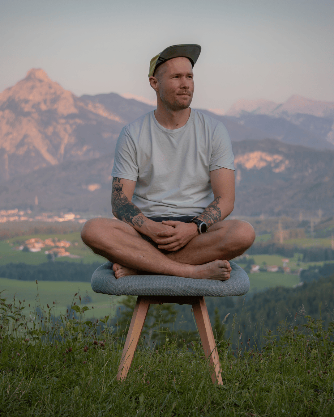 Mann sitzt im Schneidersitz auf grauem Stuhl für den Schneidersitz: vor Bergen