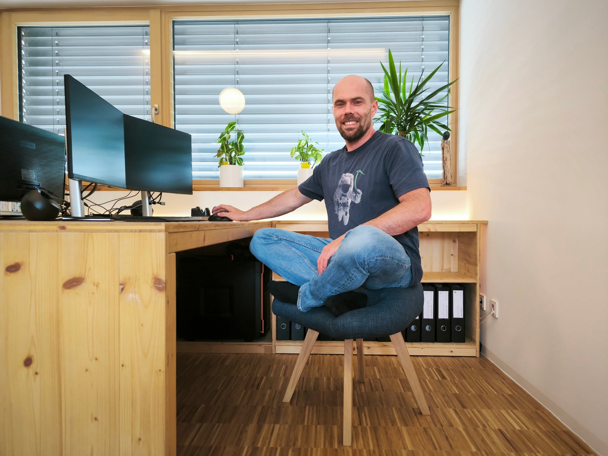 Mann sitzt auf blauem Stuhl für den Schneidersitz im Büro