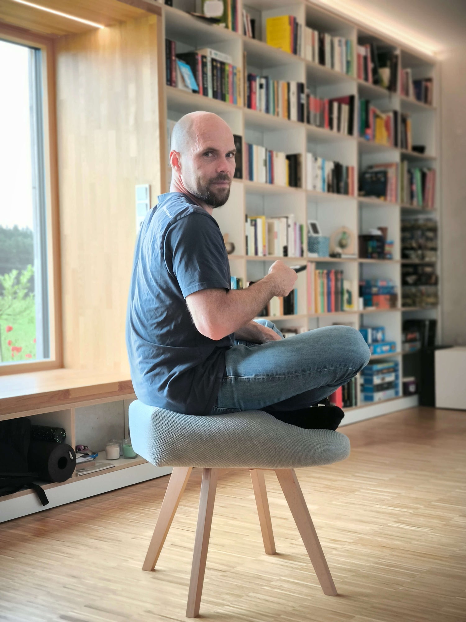 Mann sitzt im Wohnzimmer auf grauem Stuhl für den Schneidersitz